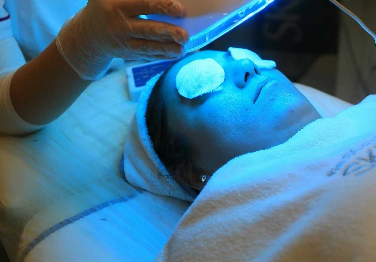 Person undergoing a facial treatment with LED blue light therapy and eyes covered.