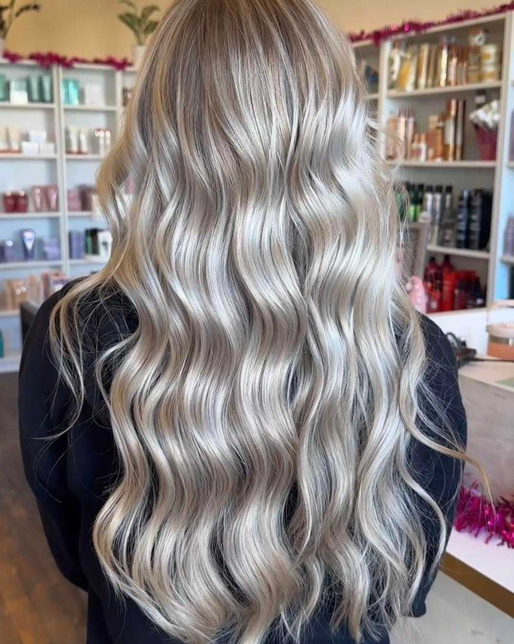 Long, wavy platinum blonde hair styled in loose curls, showcased in a bright salon setting.