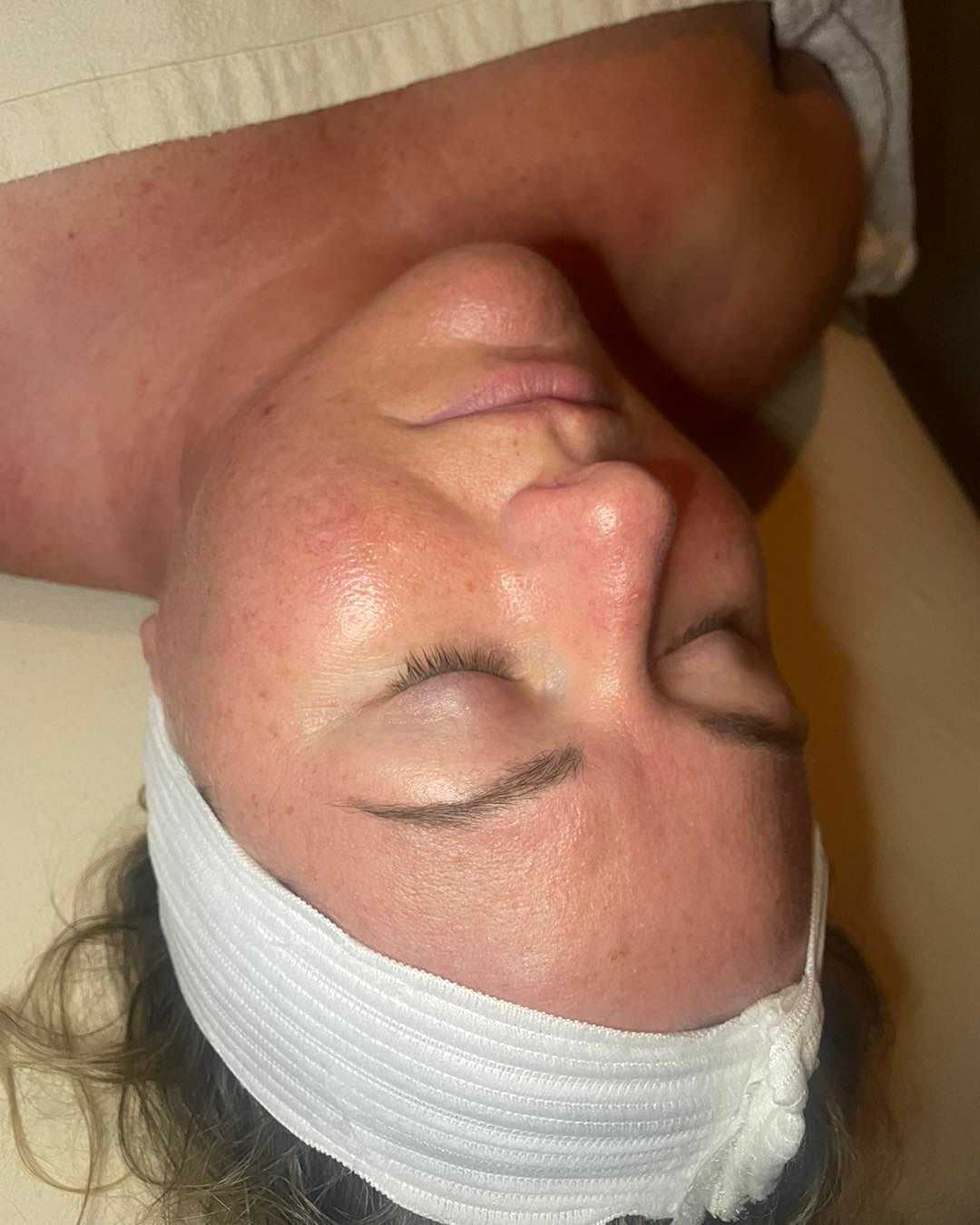 Person lying on a spa bed with a headband, eyes closed, receiving a facial treatment.