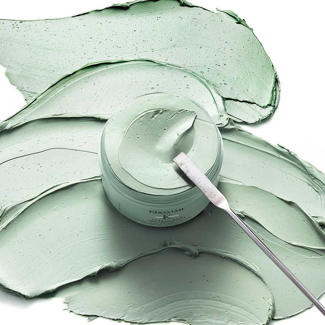 Jar of green skincare product with a spatula, shown with smooth, creamy texture spread around.