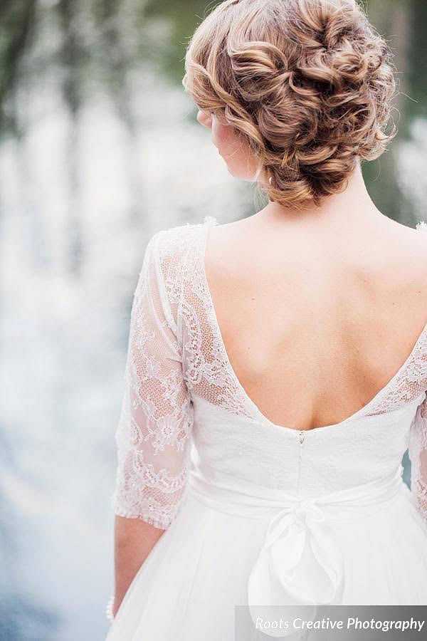 Bride in a lace wedding dress with an open back, facing away, with styled hair.
