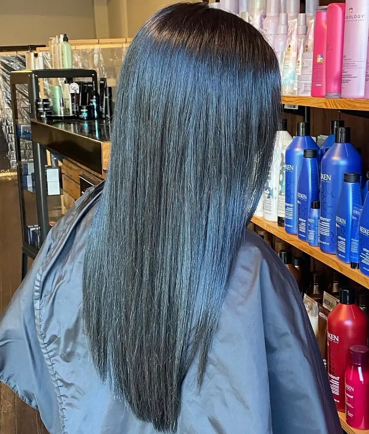 Woman with straight, shiny hair in a salon, surrounded by hair products on shelves.