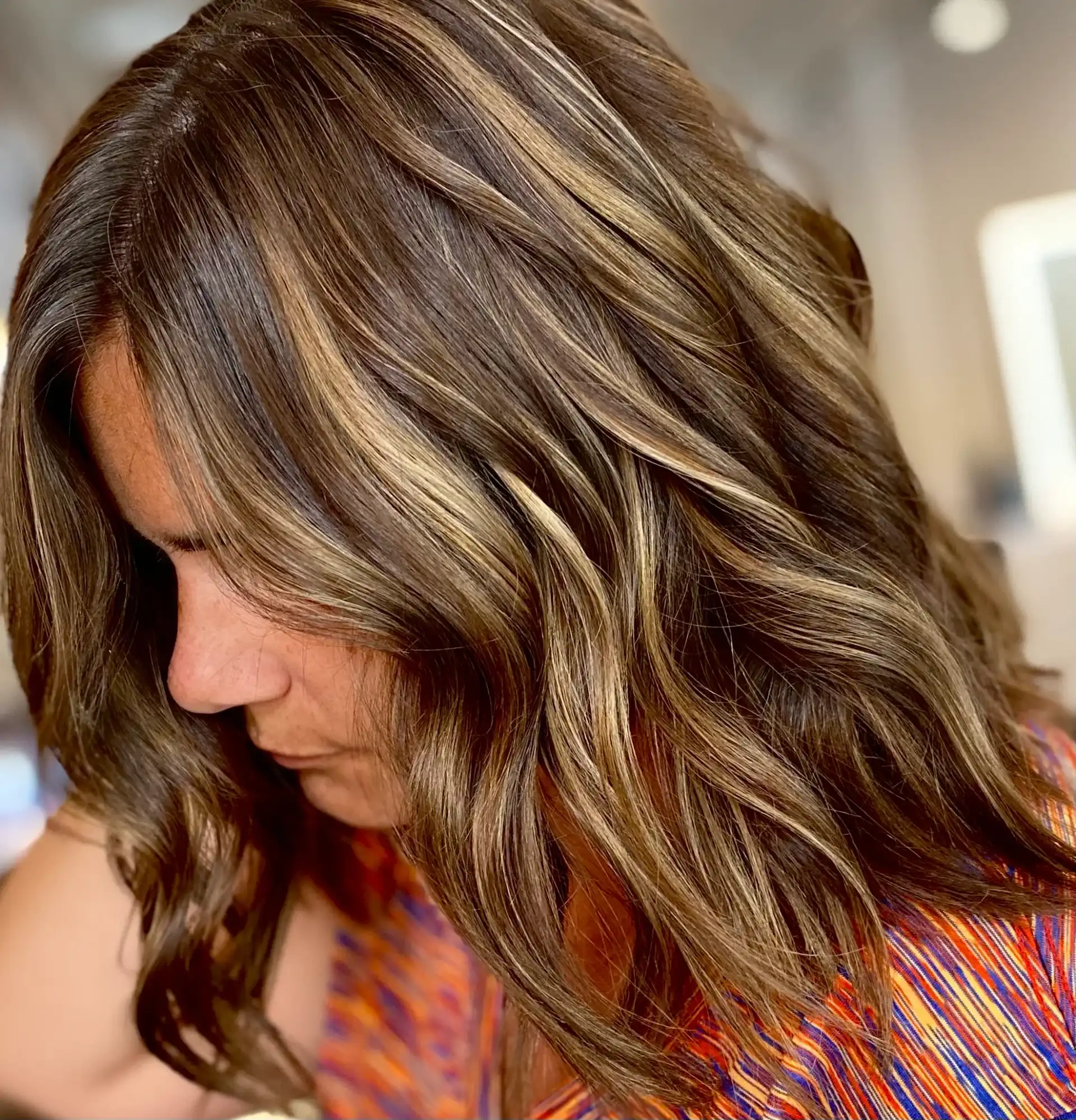 Woman with wavy brown hair highlighted with blonde streaks, head inclined downwards.