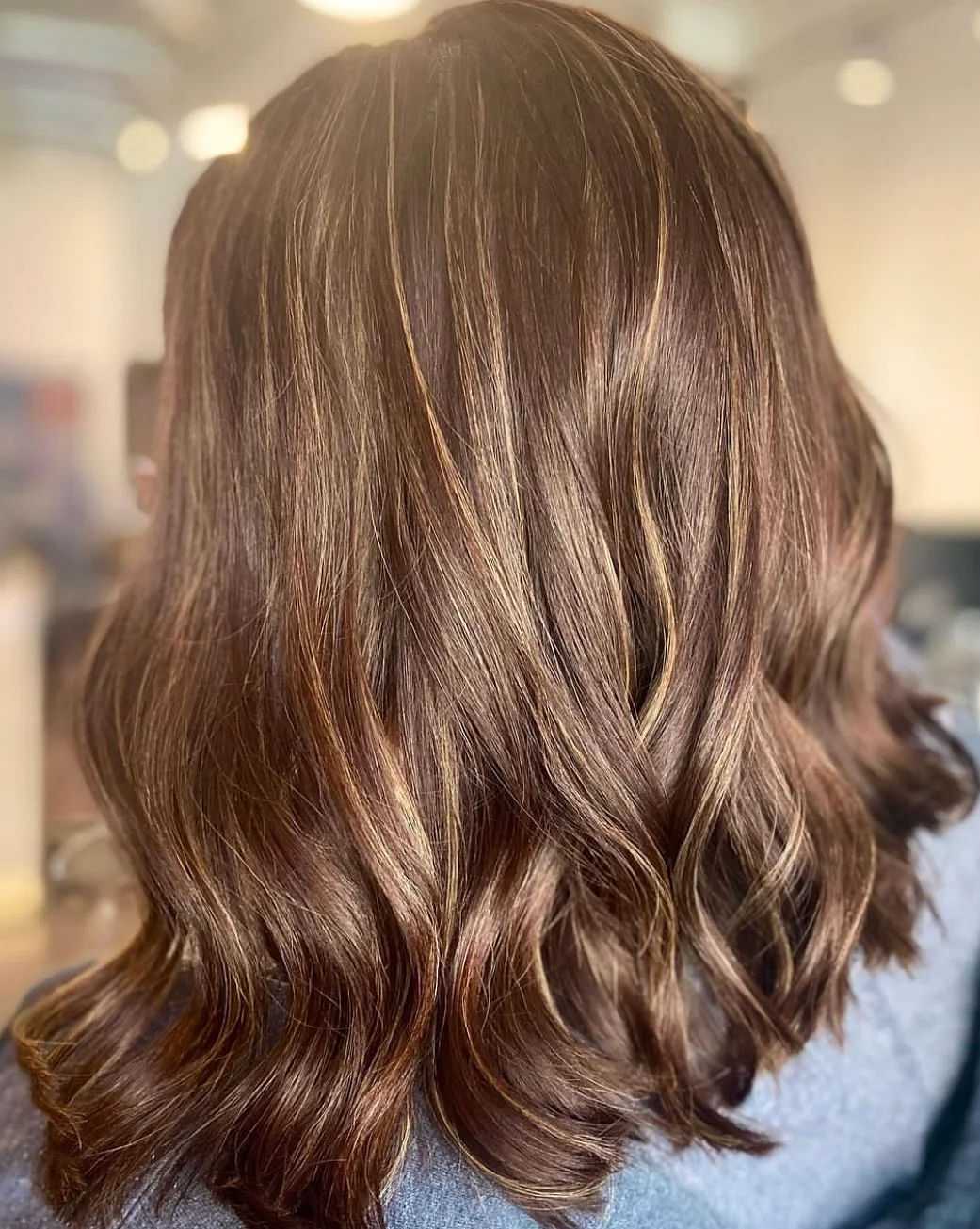 Wavy brown hair with blonde highlights, shown from the back in a well-lit salon setting.