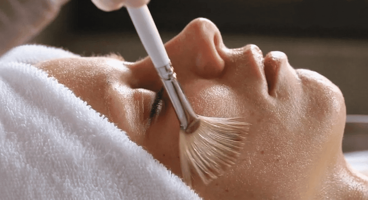 Close-up of a person receiving a facial treatment with a soft brush at a spa.